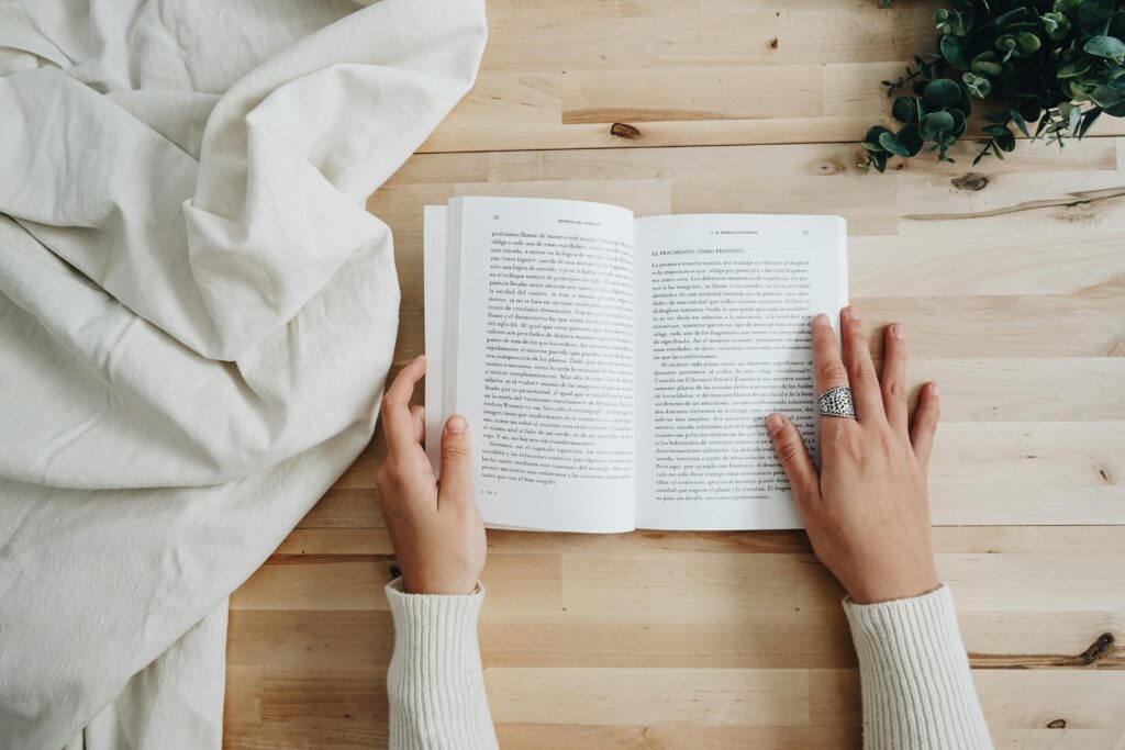 pexels photo 2663851 2663851 Top view of a person reading a book on a wooden table with a cozy setup, ideal for leisure and learning concepts.