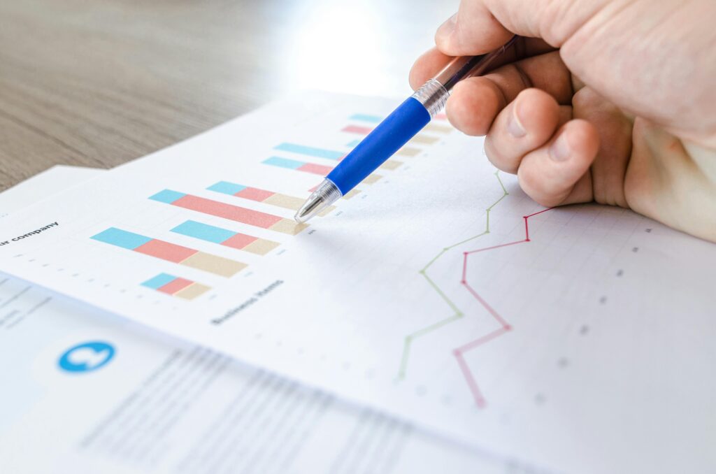 pexels photo 590022 590022 A close-up of a hand with a pen analyzing data on colorful bar and line charts on paper.