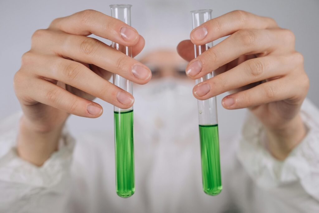 pexels photo 9243427 9243427 Close-up of hands holding test tubes with green liquid in a laboratory setting.